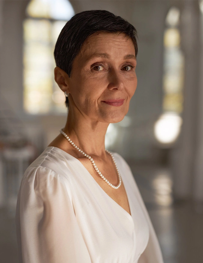 Professional woman in white blouse with pearl necklace smiling at camera in bright office setting