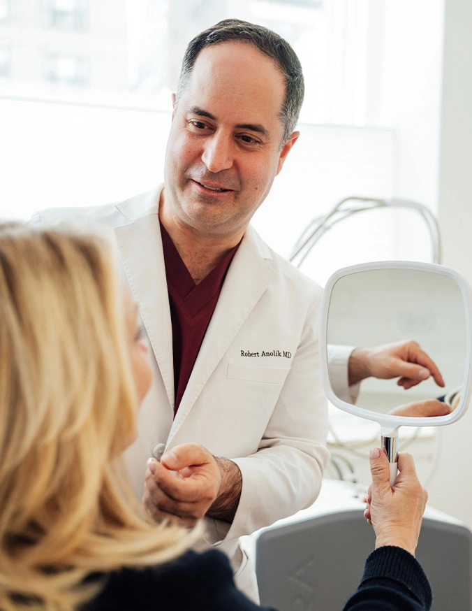 Doctor consulting with female patient about cosmetic procedure using mirror in medical office