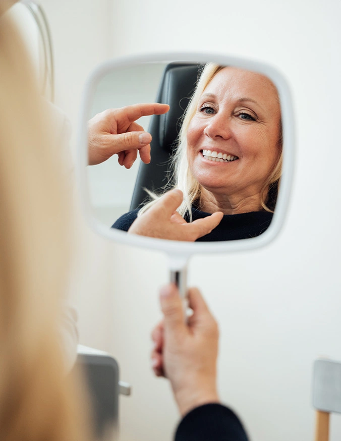 Woman smiling at reflection in handheld mirror while examining her face and skin
