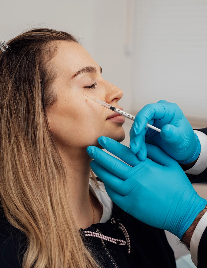Woman receiving lip filler injection from medical professional wearing blue gloves in clinical setting