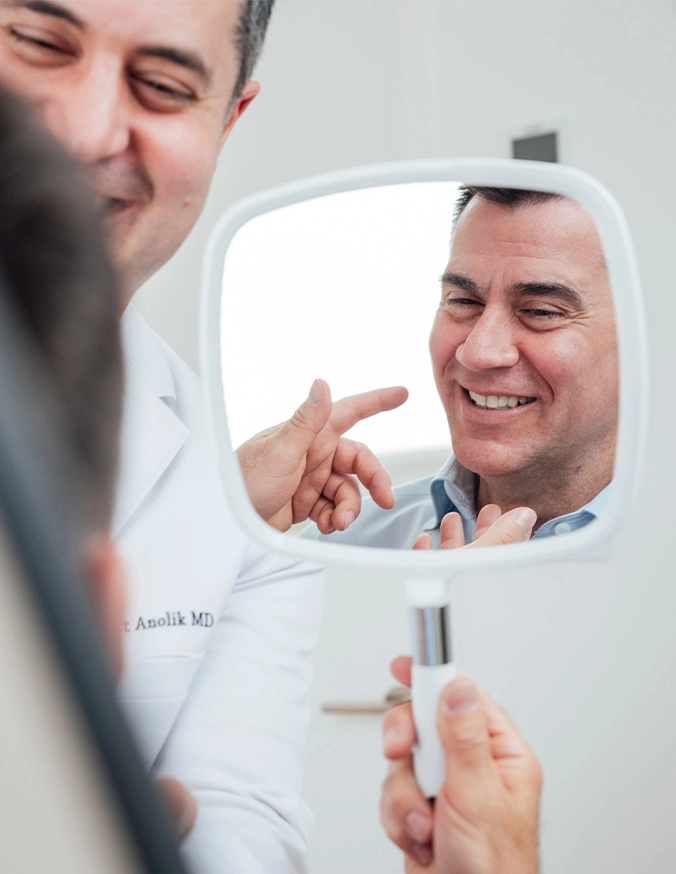 Man examining his smile in mirror while pointing at teeth during dental consultation