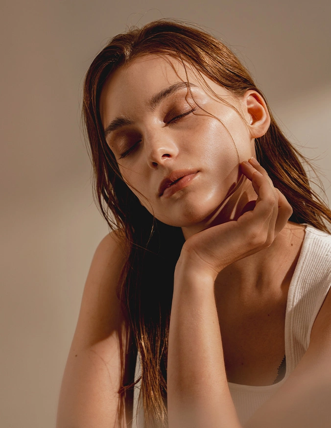 Woman with glowing skin touching face gently, demonstrating natural beauty and skincare routine in soft lighting
