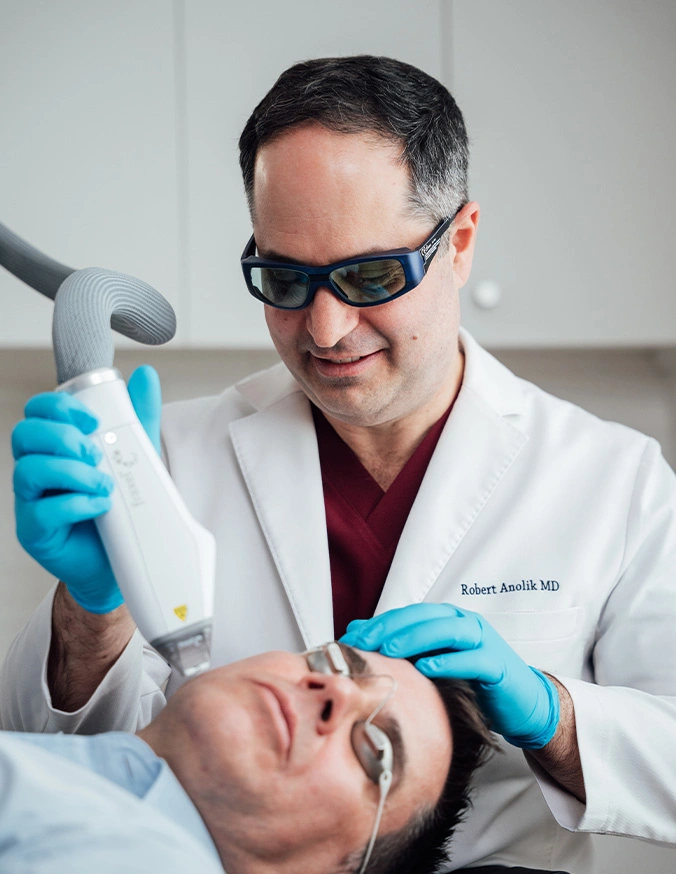 Doctor performing laser skin treatment on female patient in medical office wearing protective eyewear