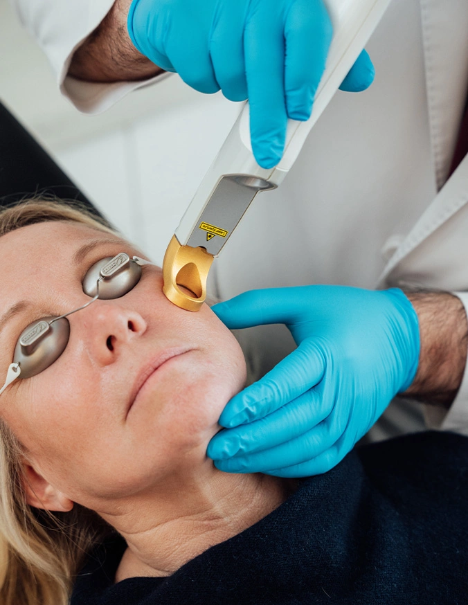 Woman receiving microneedling facial treatment from aesthetician wearing blue gloves in clinical setting