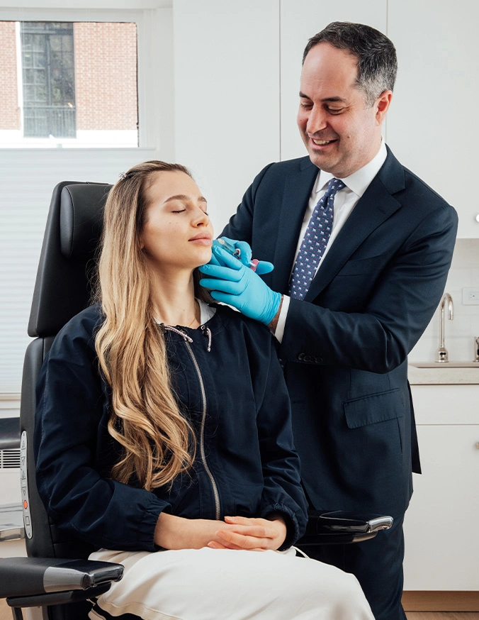 Cosmetic surgeon examining patient's face while wearing blue medical gloves in modern clinic office