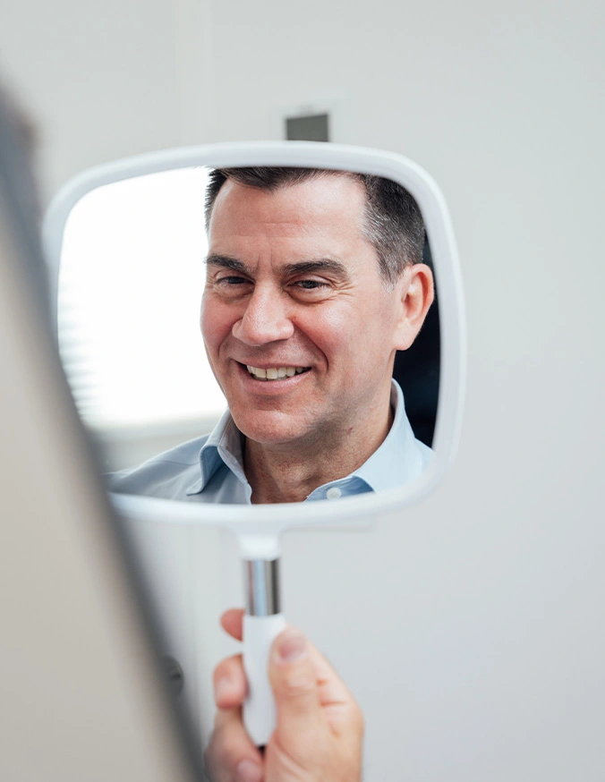 Man smiling at his reflection in a handheld mirror, showing positive self-image and confidence