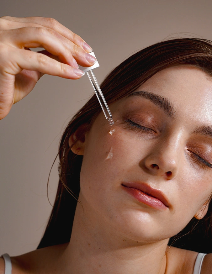 Woman applying facial serum with dropper to face during skincare routine