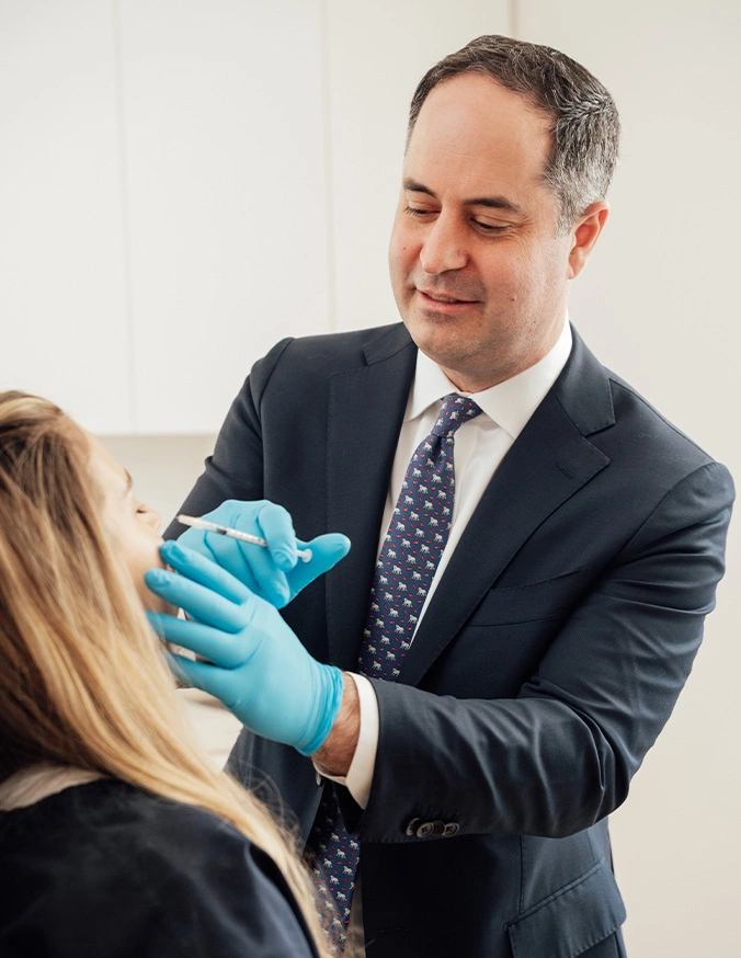 Medical professional in suit and blue gloves examining patient's face during cosmetic consultation
