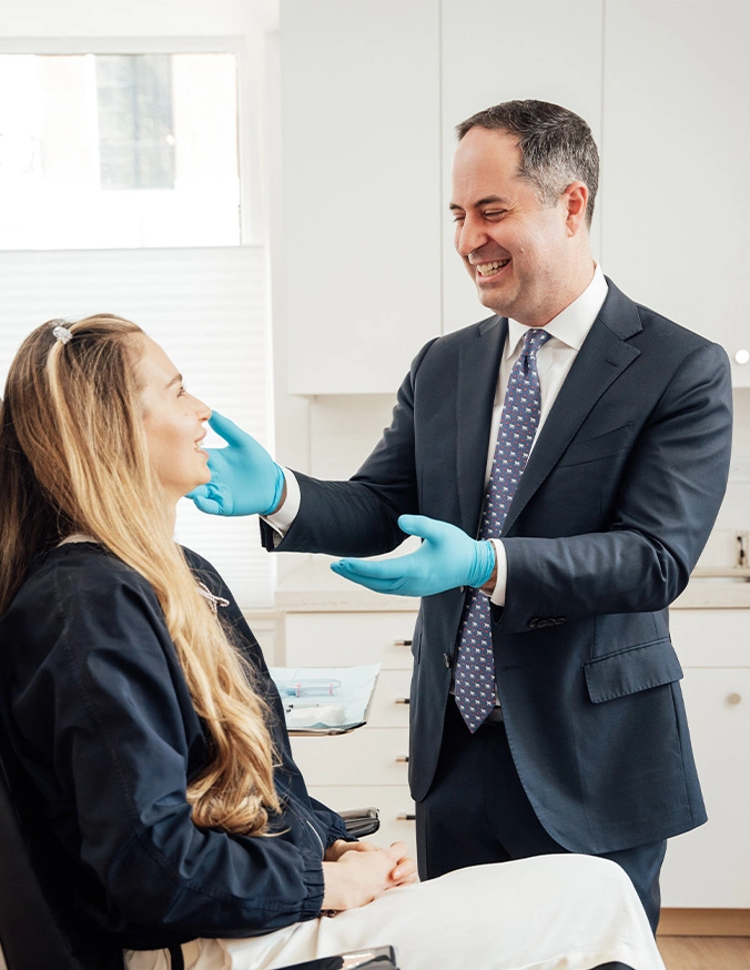 Dentist examining female patient's face while wearing blue gloves in modern dental office
