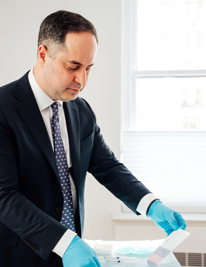 Professional man in suit wearing blue medical gloves examining documents at desk in bright office setting
