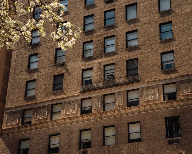 Brick apartment building facade with rows of windows and decorative stone details beneath spring blossoms