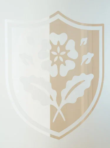 Shield emblem with floral design featuring rose and leaves in beige and white tones