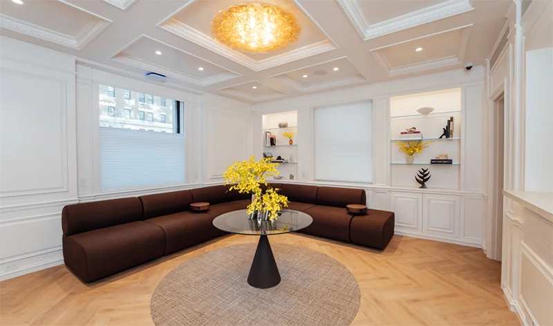 Modern basement living room with brown sectional sofa, round rug, white walls, and elegant ceiling light fixture