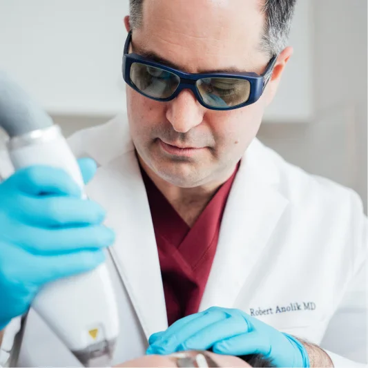 Surgeon wearing protective eyewear and blue gloves examining medical equipment in laboratory setting