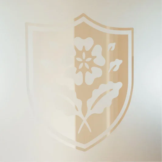 Shield emblem with floral design etched in beige and white tones on neutral background