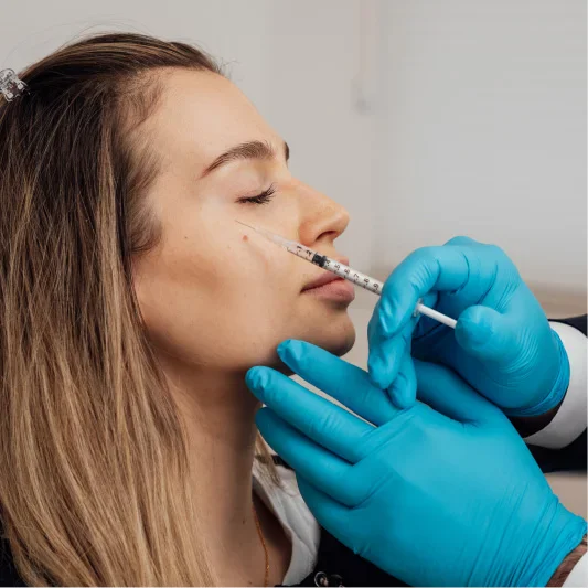 Woman receiving nasal injection from medical professional wearing blue gloves during cosmetic procedure
