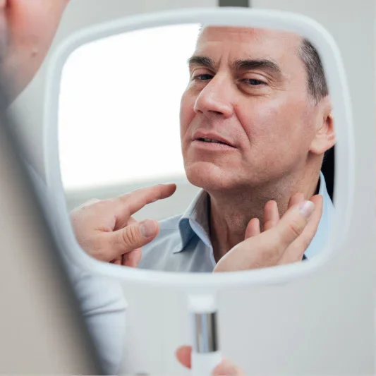 Man examining neck in mirror during self-assessment consultation with surgeon