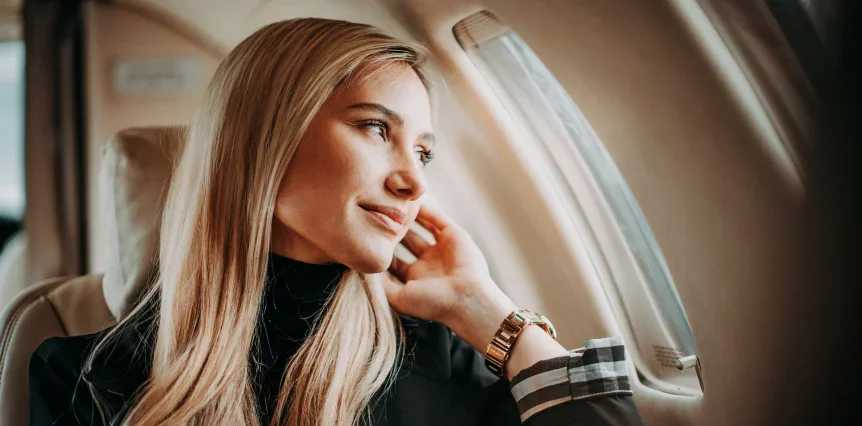 Woman gazing thoughtfully out airplane window during flight, blonde hair, natural light